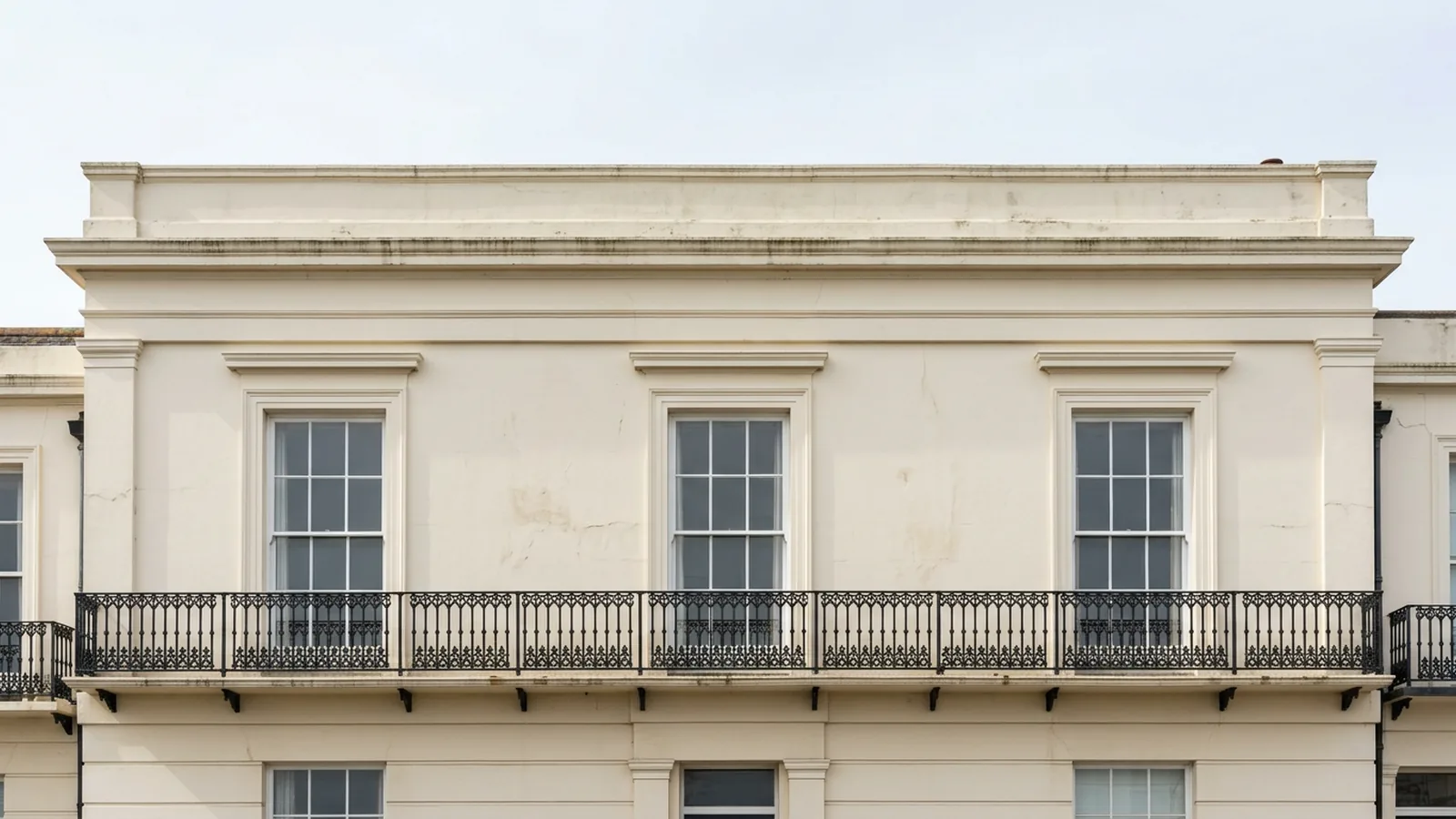 Three tall white sash windows above a black iron balcony on a stucco facade